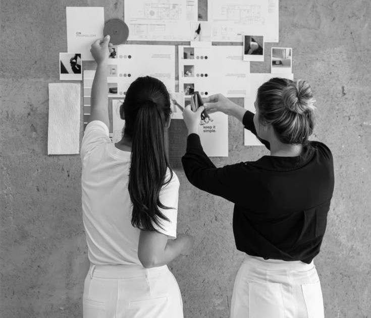 Two creatives arranging references on a studio wall