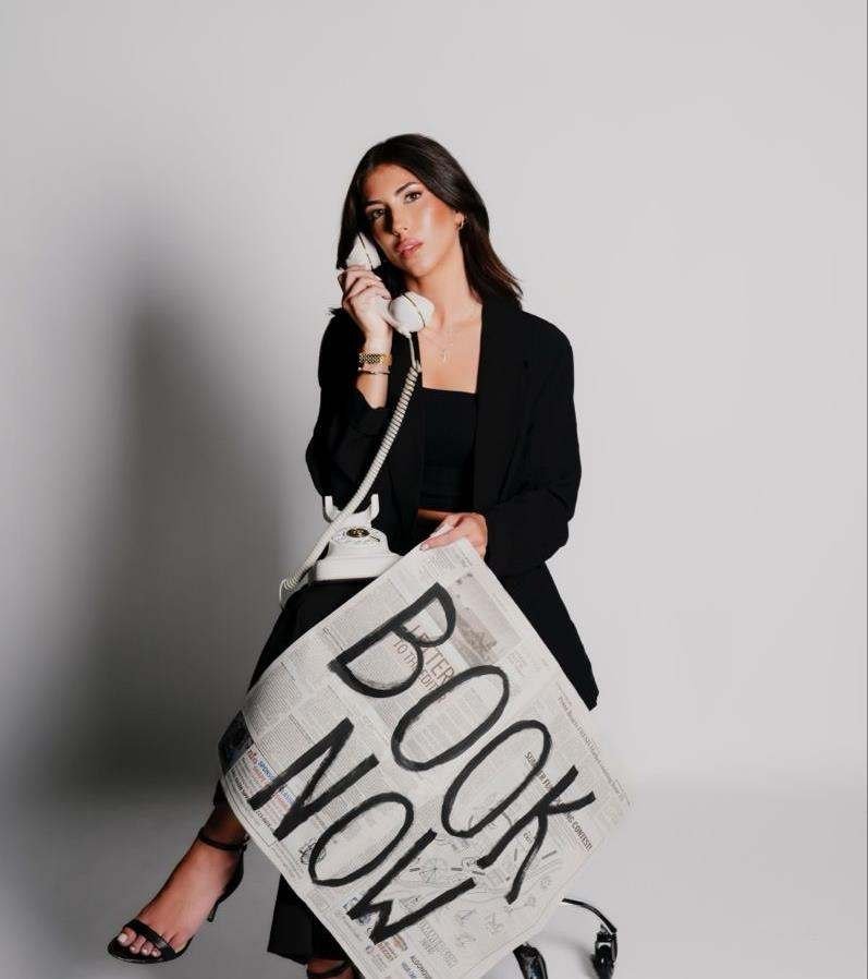 Woman in black tailoring holding a telephone beside a handwritten sign